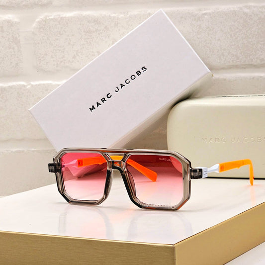 Sunglasses with red and orange gradient lenses on a white surface with Marc Jacobs packaging.
